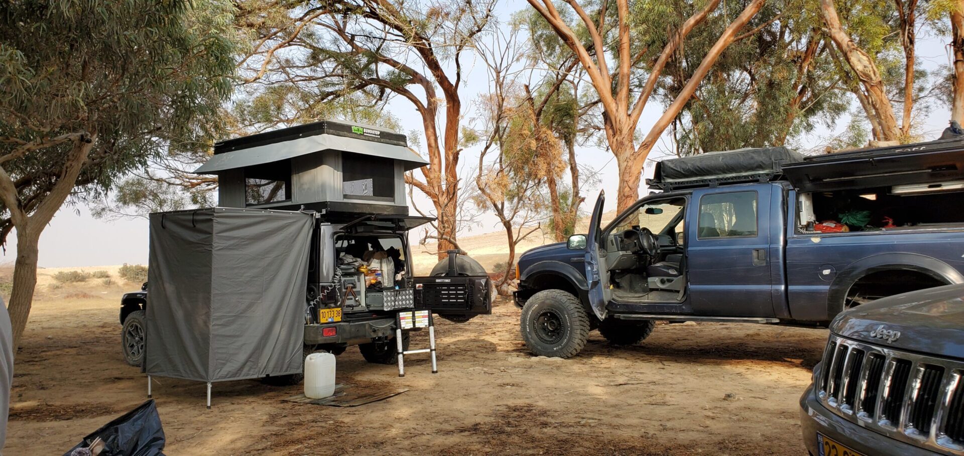 A truck and camper in the dirt near trees.
