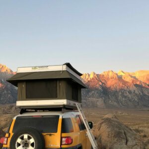 A yellow suv with an open roof and ladder.