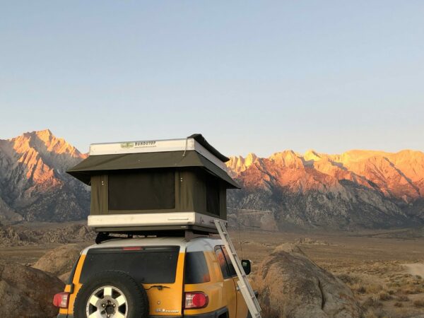 A yellow suv with an open roof and ladder.