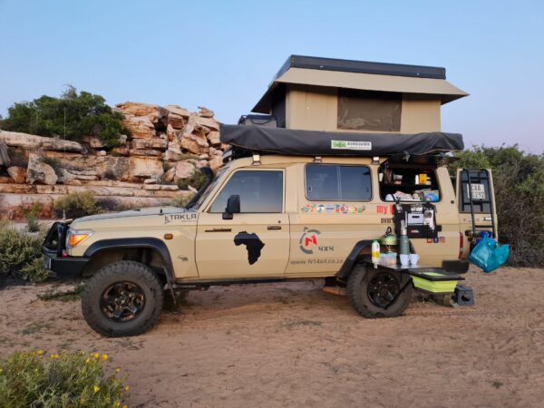 A tan truck with a tent on top parked in the dirt.