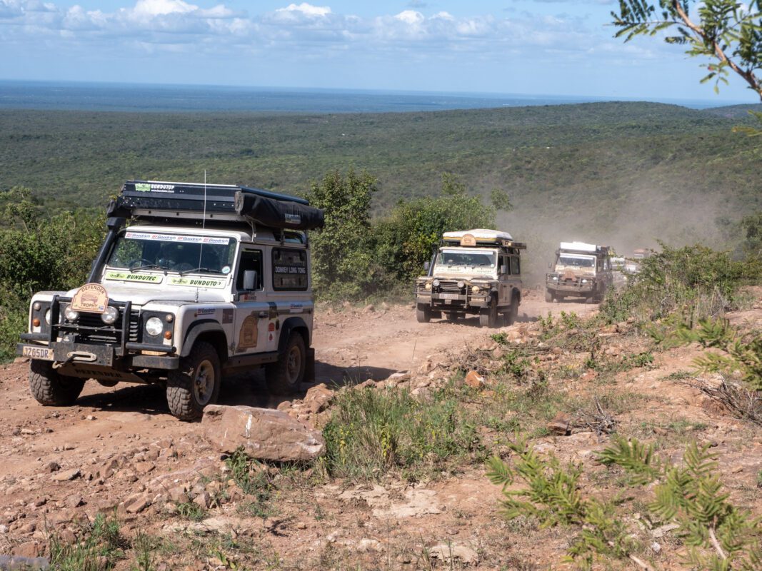 A group of four off road vehicles driving on the side of a hill.