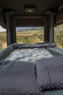 A bed in the back of a truck with a view out the window.