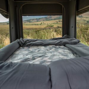 A bed in the back of a truck with a view out the window.