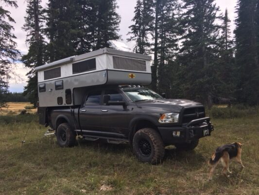 A truck with an rv on the back in a field.