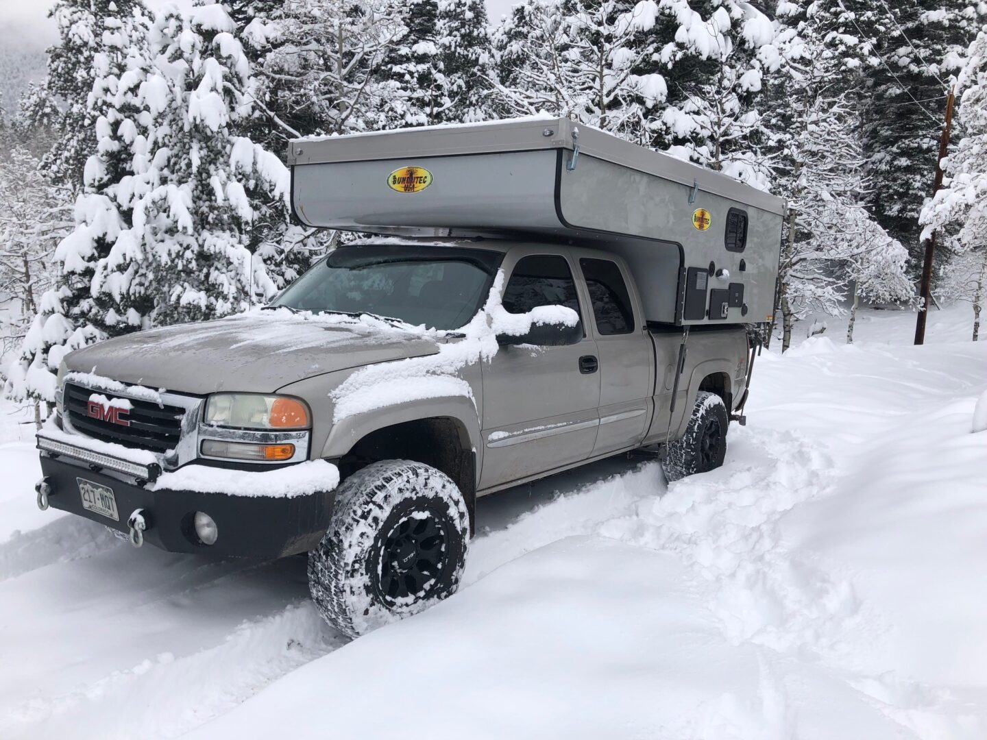 A truck with an rv in the back is parked on snow.