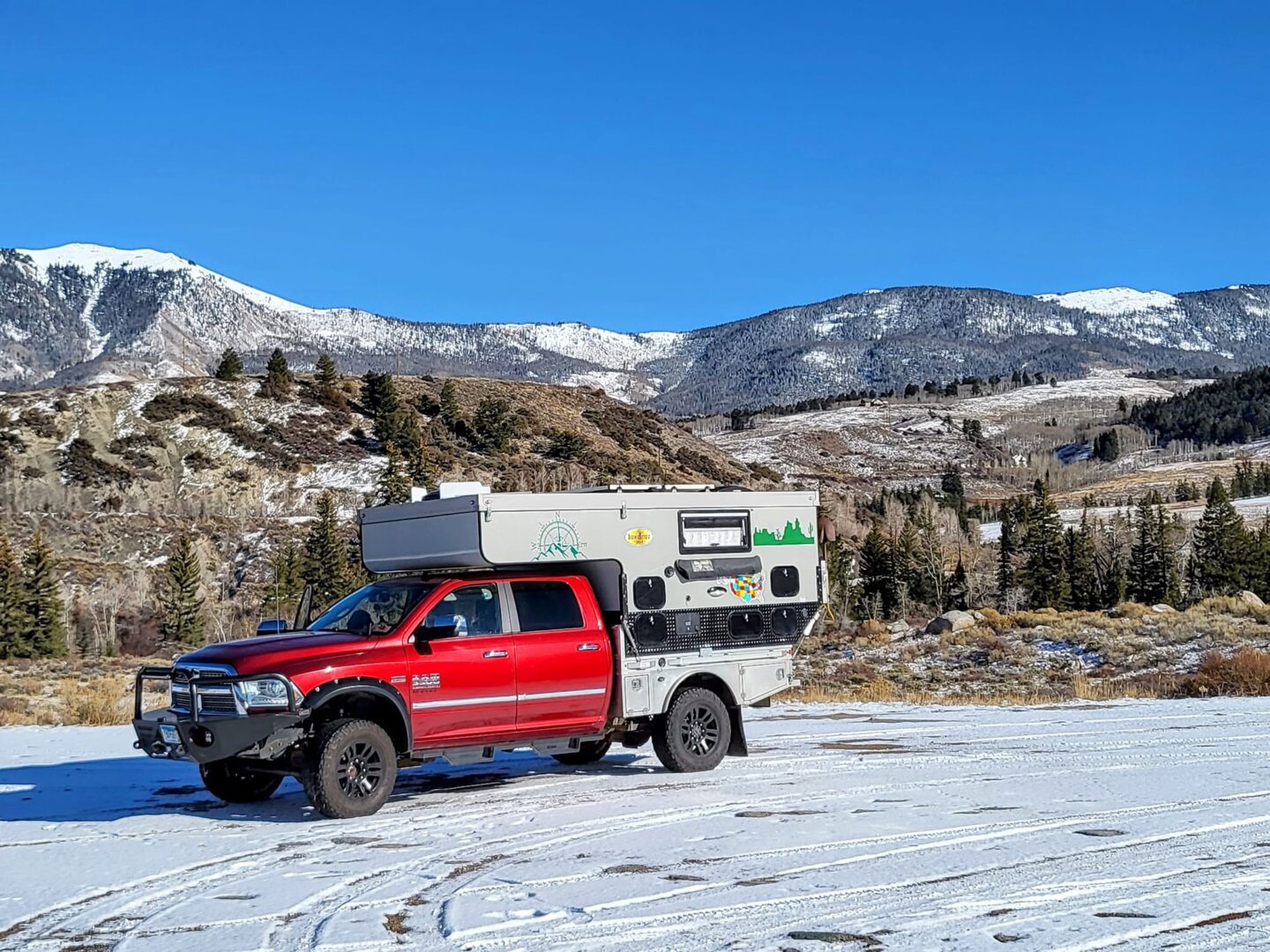 A red truck parked in the snow with an rv trailer.