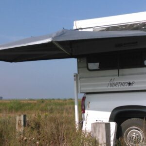 A white bus parked in the grass under an awning.