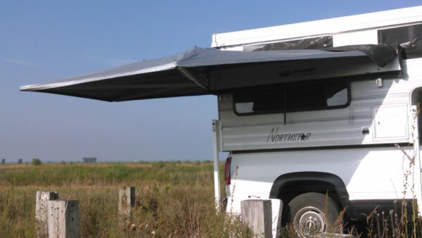 A white bus parked in the grass under an awning.