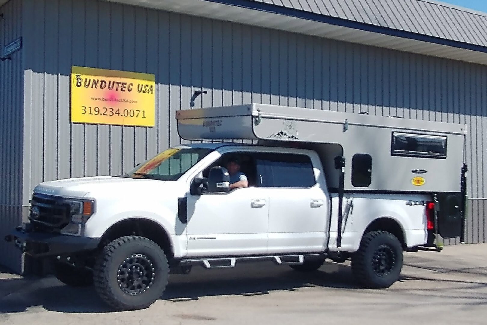 A white truck with a camper on the back of it.