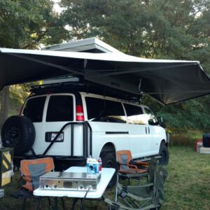 A white van with an awning and table set up for camping.