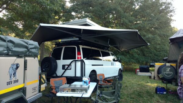 A white van with an awning and table set up for camping.