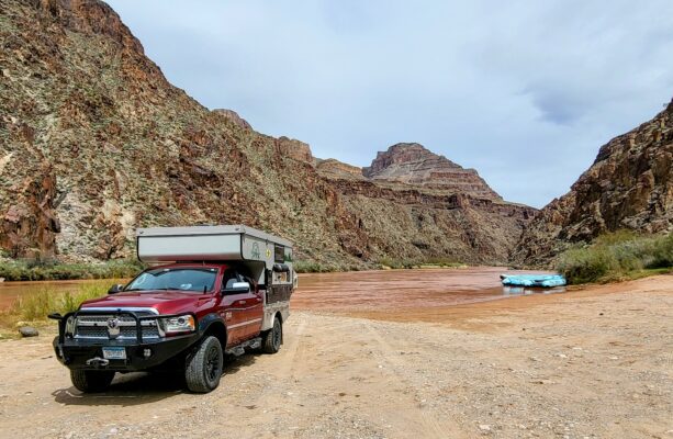 A truck with a camper on the back parked in front of some mountains.