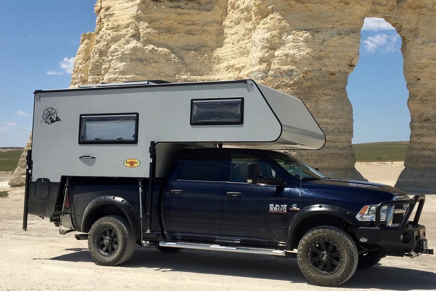 A truck with an rv on top of it parked in front of a rock formation.