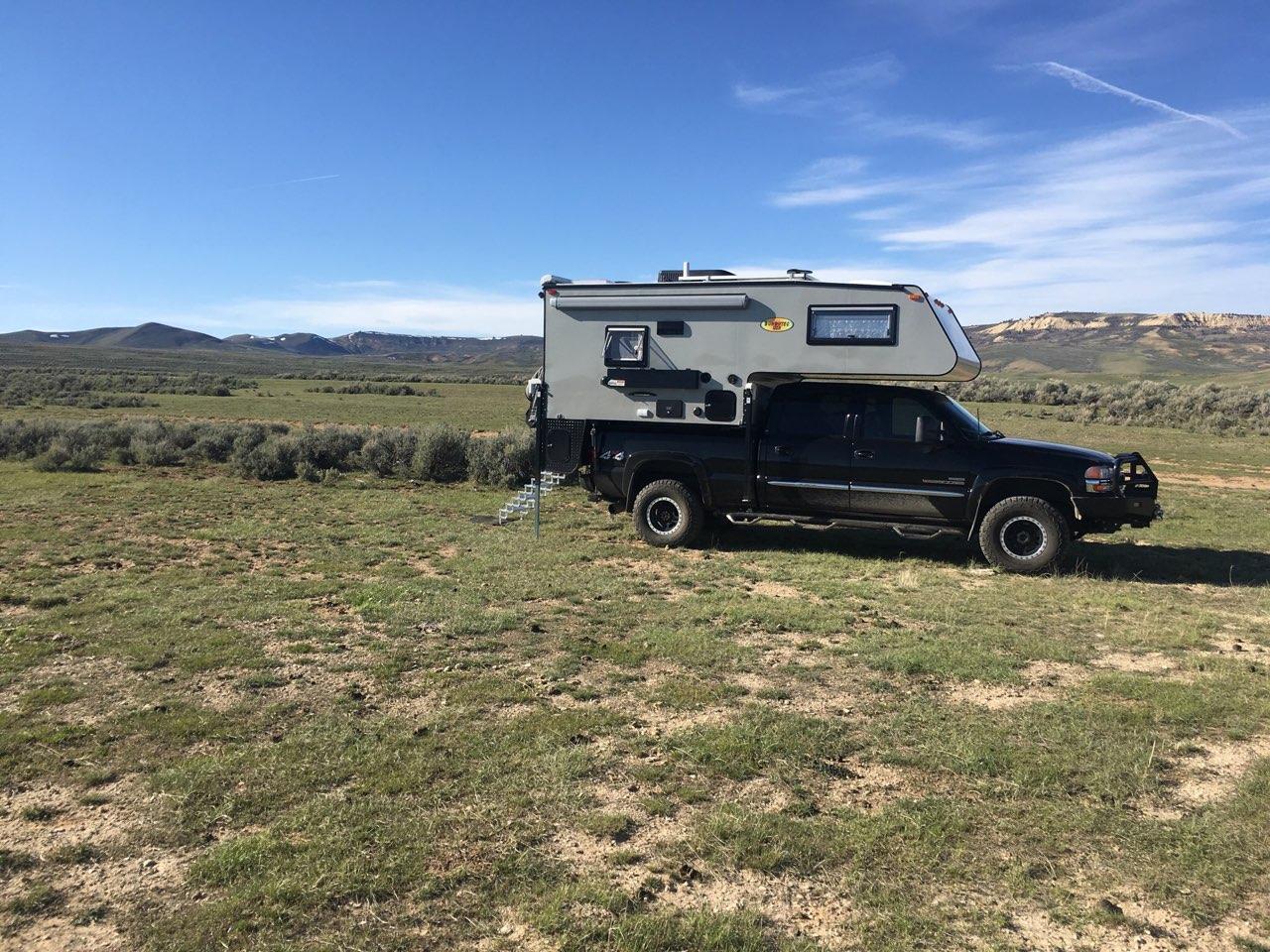 A truck parked in the grass with an rv on top of it.