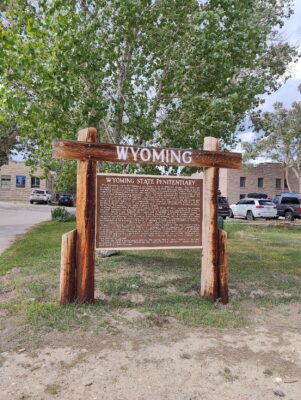 A sign in the grass with trees and cars parked on it.