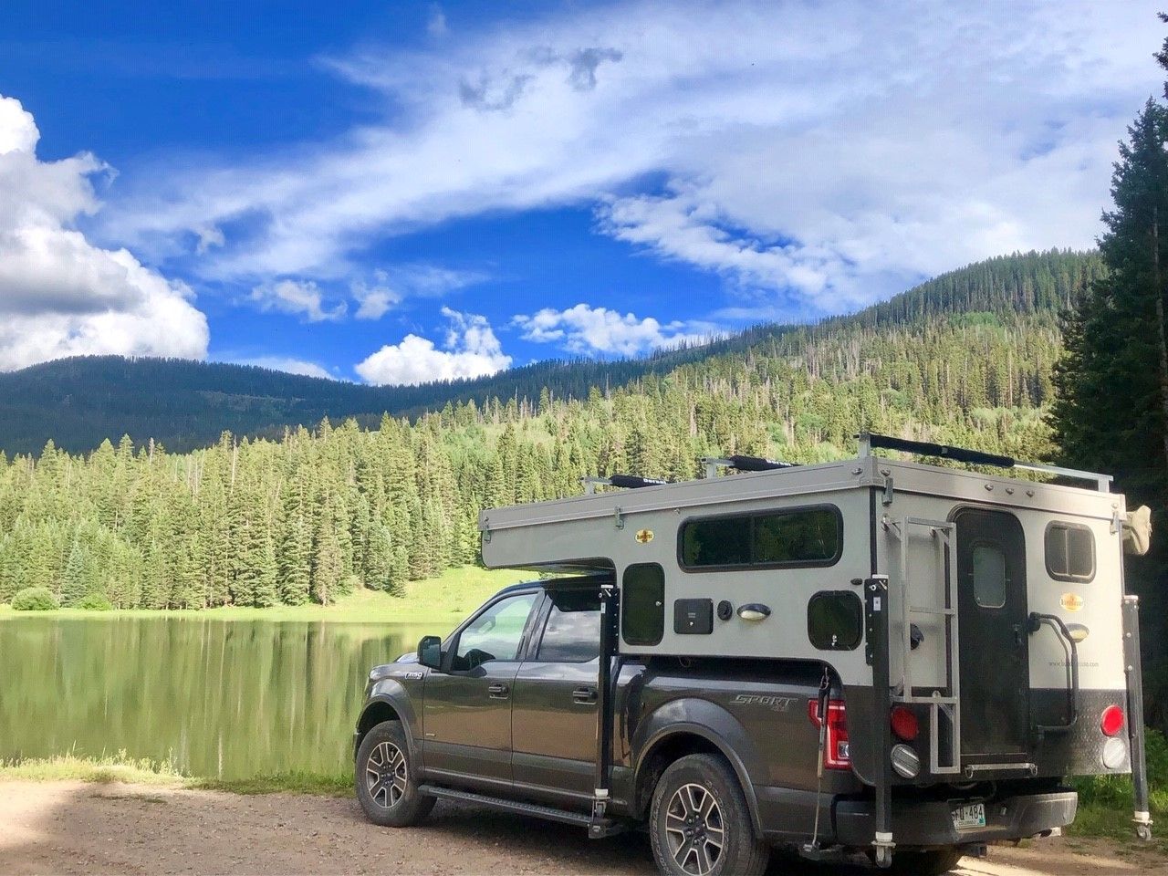 A truck with a camper parked next to a lake.