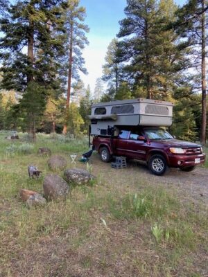 A red car parked next to a camper in a wooded area.