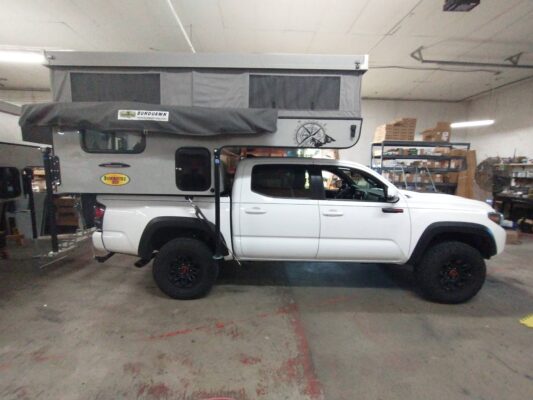 A white toyota tacoma with a camper attached to it.