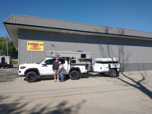 Two people standing in front of a truck and trailer.