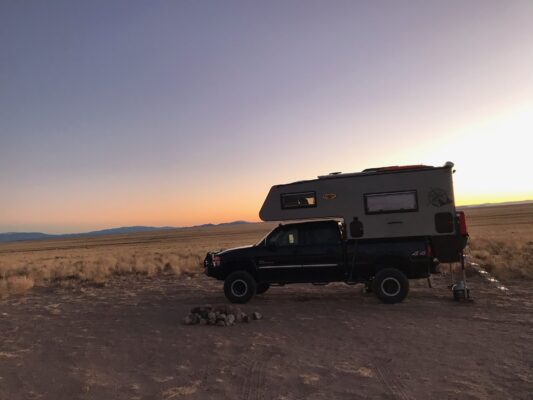 A camper truck parked in the desert at sunset.