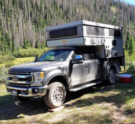 A truck with a camper parked next to a mountain.