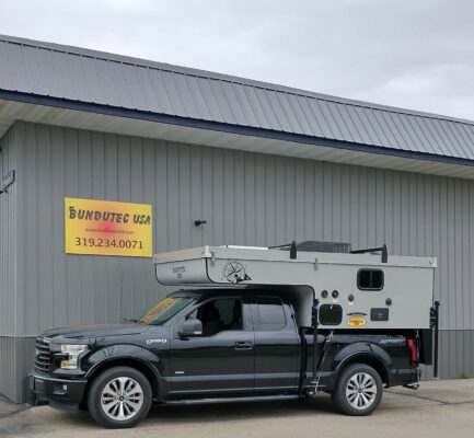 A black truck with a camper parked in front of a building.