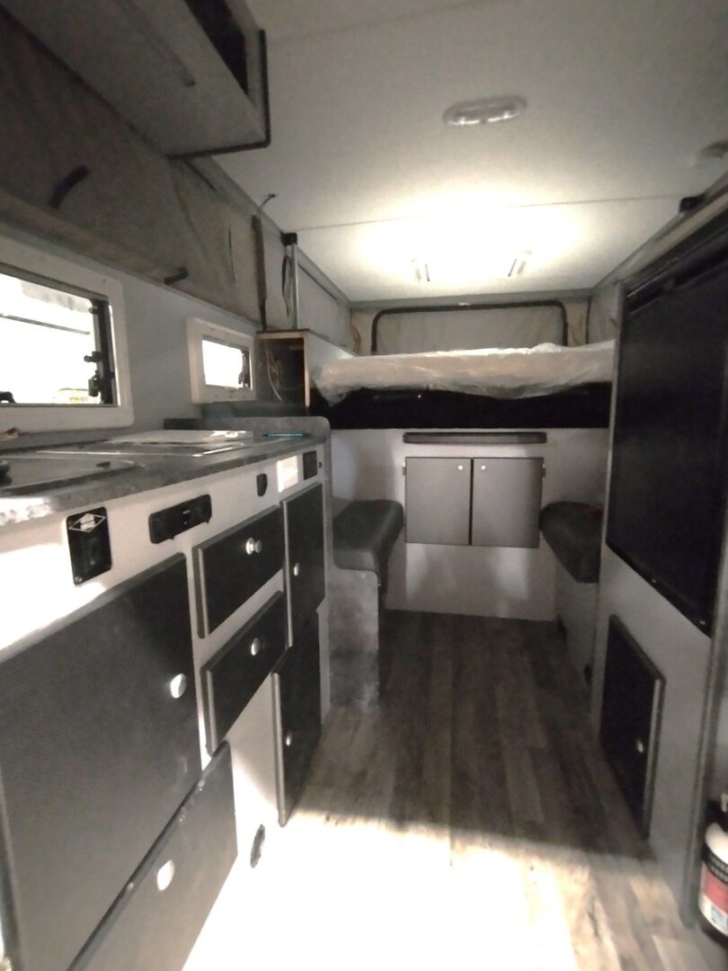 The interior of an rv with a bed and a sink.