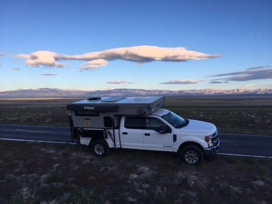 A white truck with a camper parked on the side of the road.