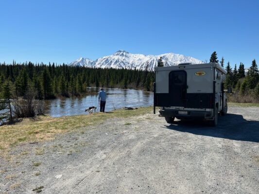 An rv parked next to a river with mountains in the background.