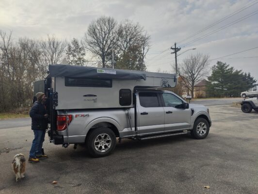 A man is standing next to a truck with a camper on top.