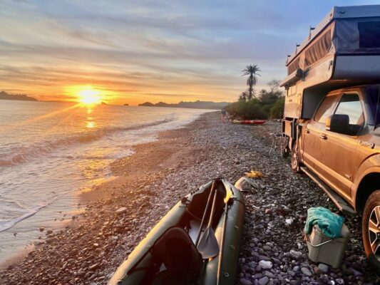 A camper is parked on the beach with a canoe next to it.