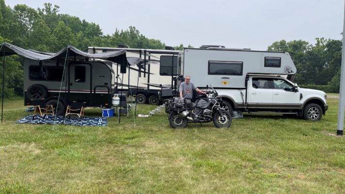 A man standing next to an rv with a motorcycle next to it.