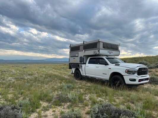 A white truck with a camper parked in the middle of a field.