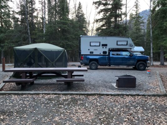 A blue truck parked next to a picnic table in a wooded area.