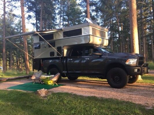 A truck with a camper parked in the woods.