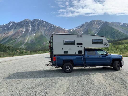 A blue truck with a camper parked on the side of the road.