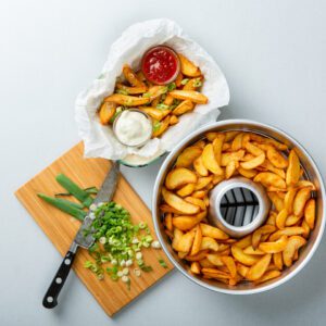 A bowl of french fries and a knife on a cutting board.