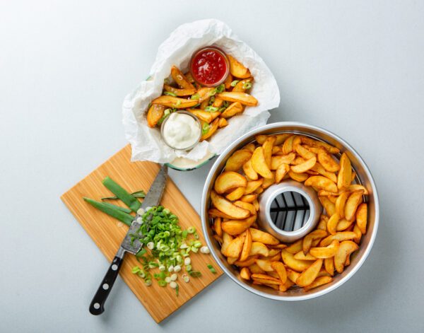 A bowl of french fries and a knife on a cutting board.