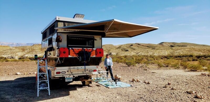 A man standing next to a camper in the desert.