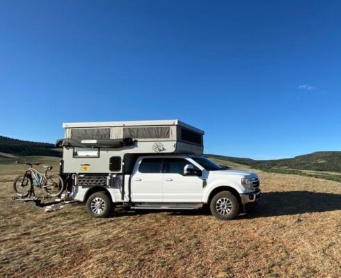 A truck with a camper parked in the middle of a field.