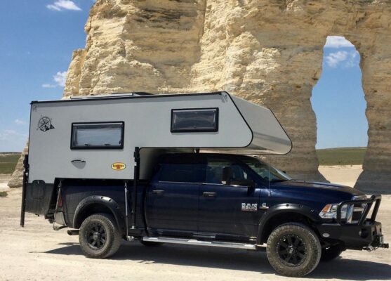 A truck with a camper parked in front of a rock formation.