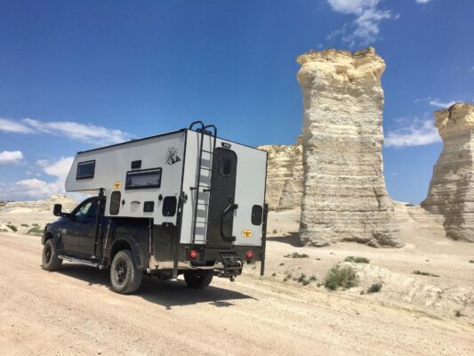 An rv parked on a dirt road near a rock formation.