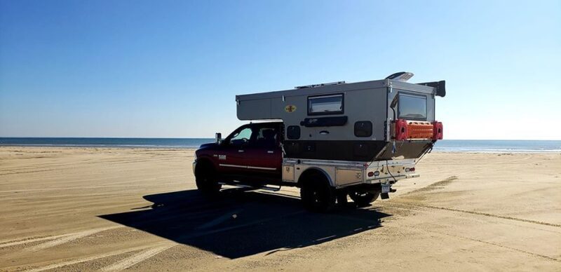 A truck parked on the beach with a camper on top.