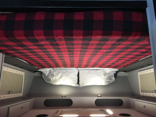 A bed in an rv with a red and black checkered blanket.