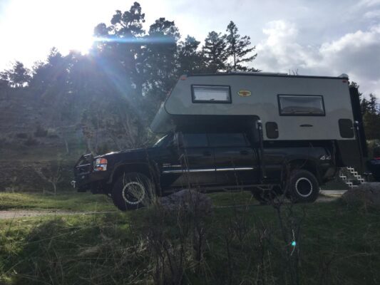 A black truck with a camper parked on the side of the road.