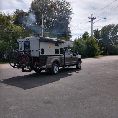 A truck with a camper and bicycles parked in a parking lot.