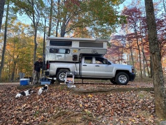 A man and his dog standing next to a camper in the woods.