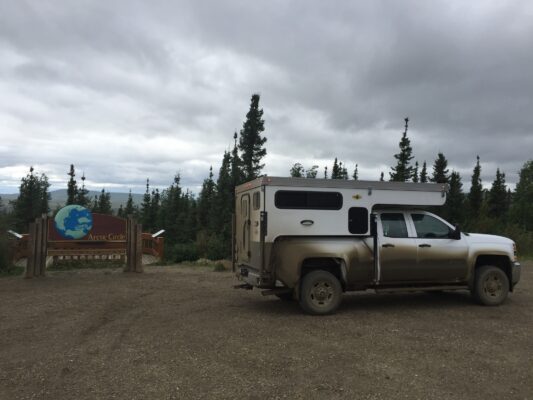 A truck with a camper parked in front of a sign.