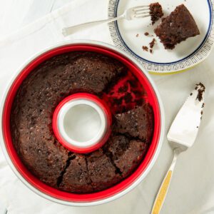 A chocolate cake in a red silicone mold with a slice missing.