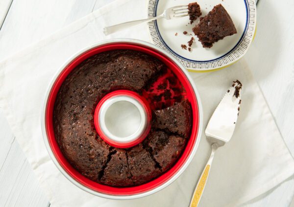 A chocolate cake in a red silicone mold with a slice missing.